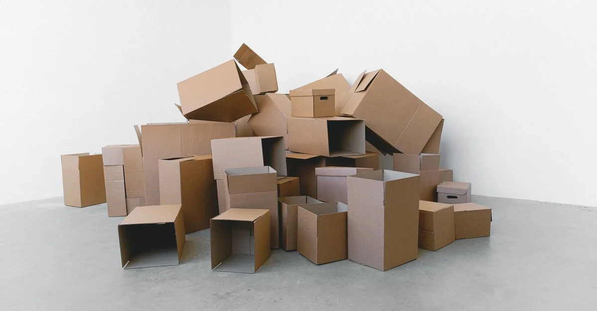 Un montón de cajas de cartón vacías organizadas sobre un suelo gris contra una pared blanca, perfecto para temas de mudanza.
