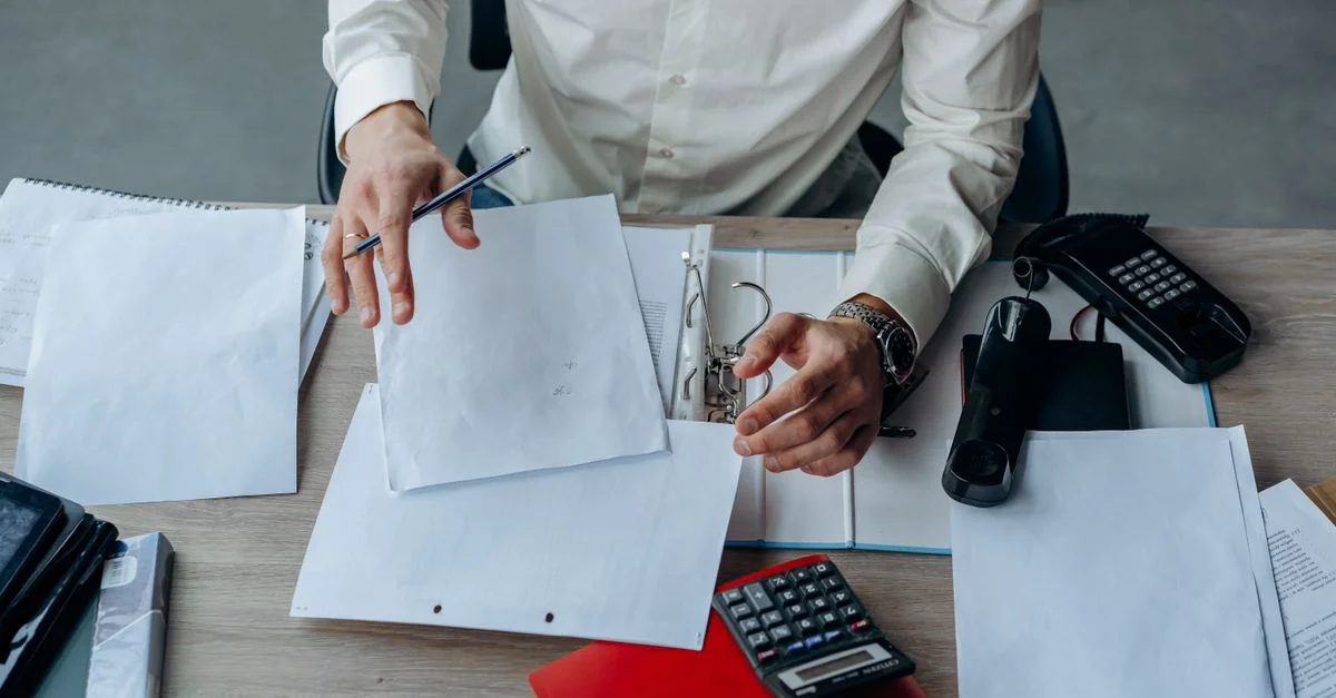 Un profesional de negocios organizando documentos en un escritorio ocupado, enfatizando la productividad.
