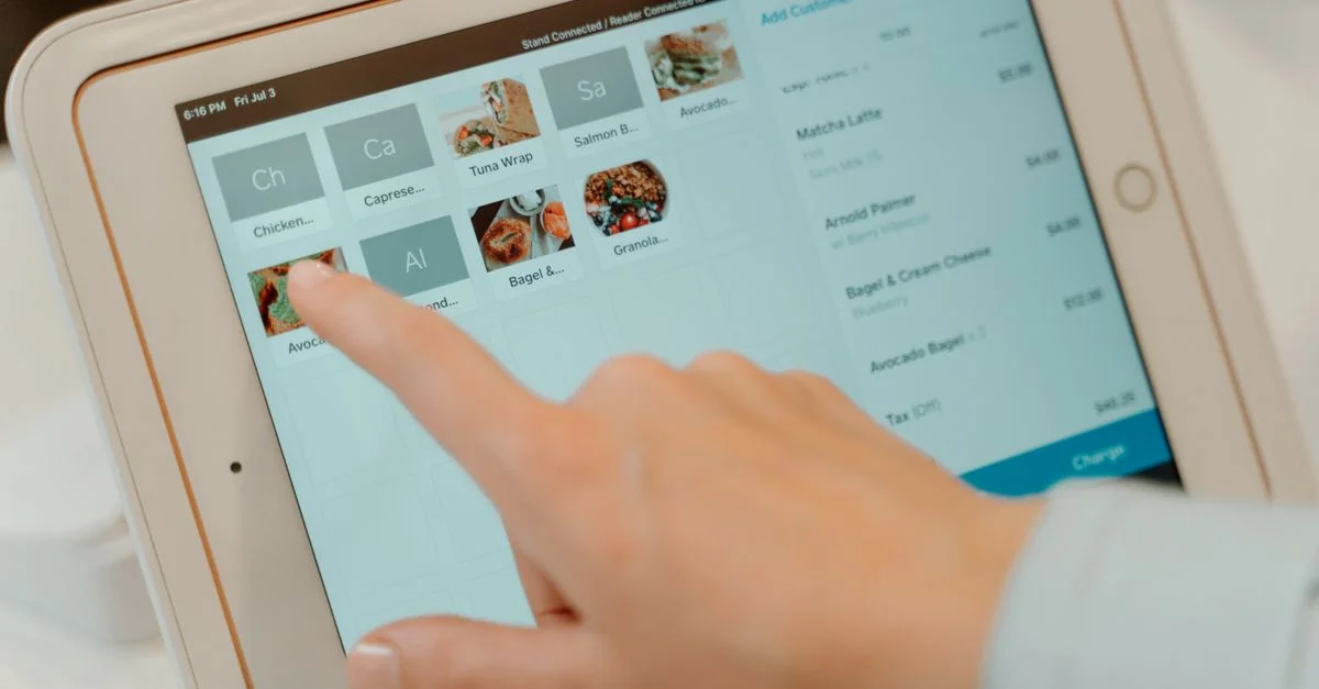 Dedo tocando la pantalla de una tableta para seleccionar artículos de comida en un ambiente de restaurante.