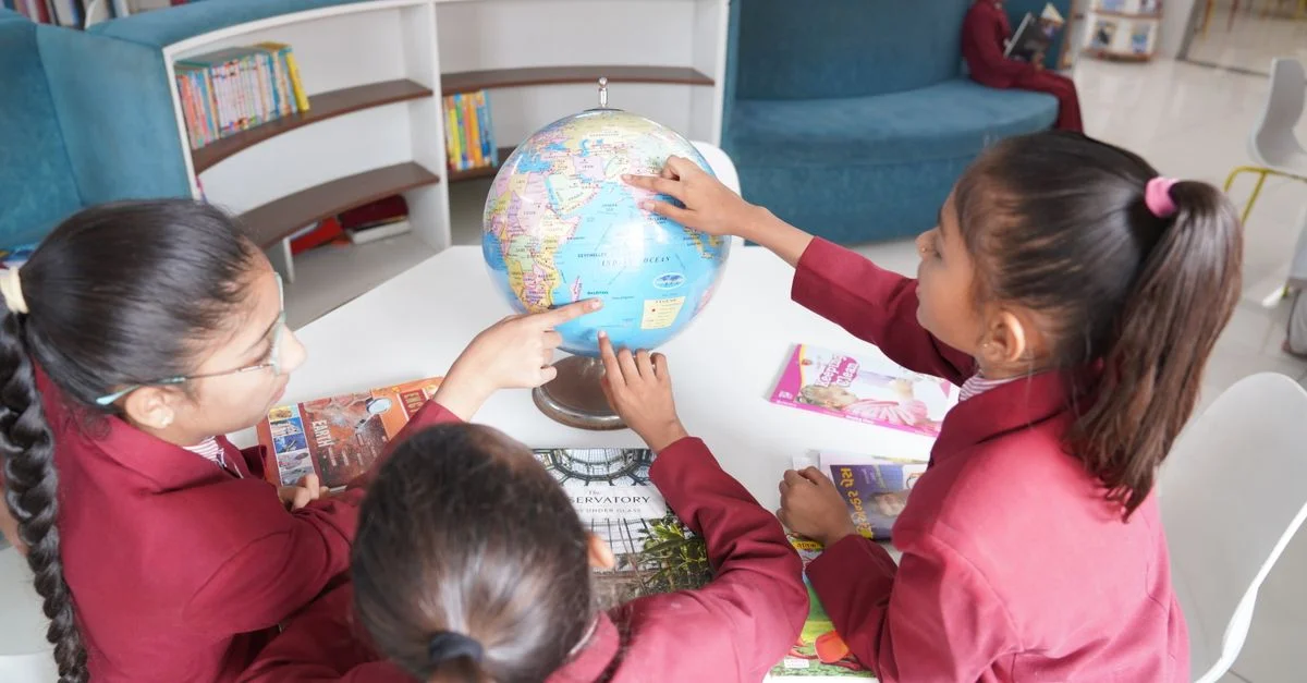Niños uniformados aprenden geografía con un globo terráqueo en una biblioteca contemporánea.