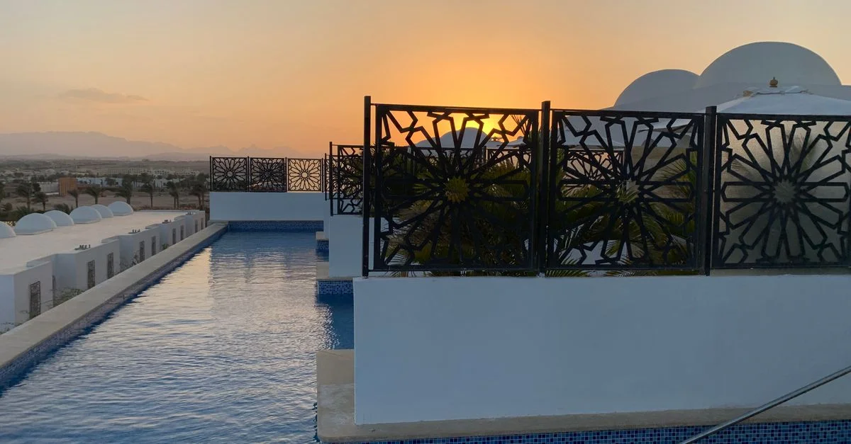 Tranquila piscina infinita con una valla ornamentada, con vistas a una pintoresca puesta de sol en Egipto.