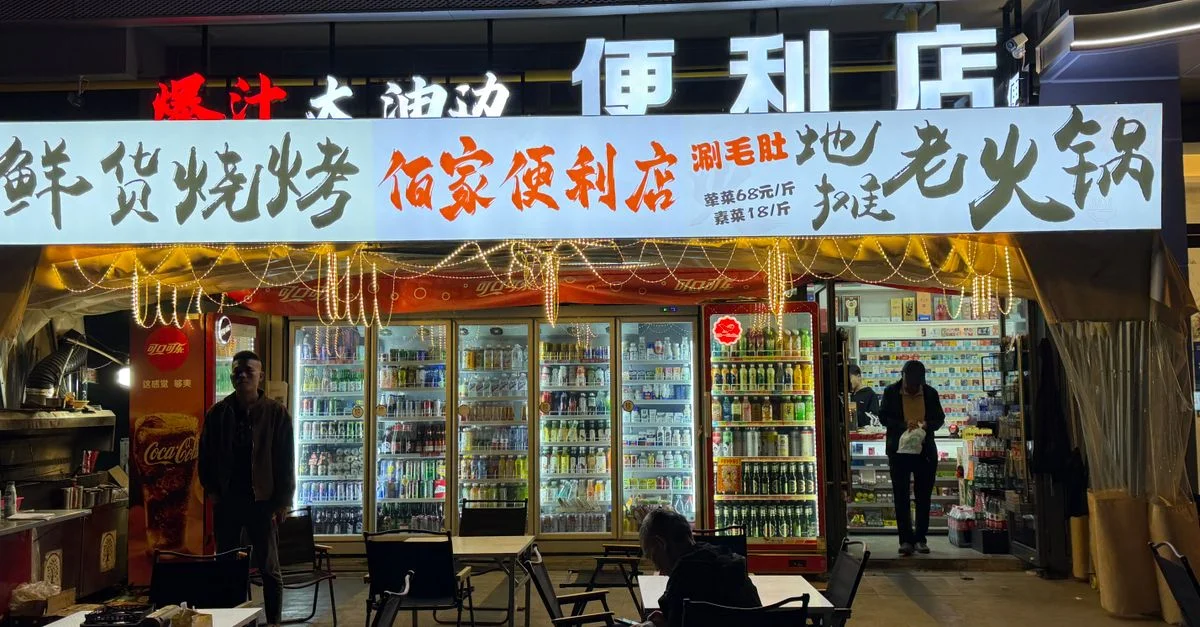 Tienda de conveniencia iluminada por la noche con gente comprando y comiendo afuera.