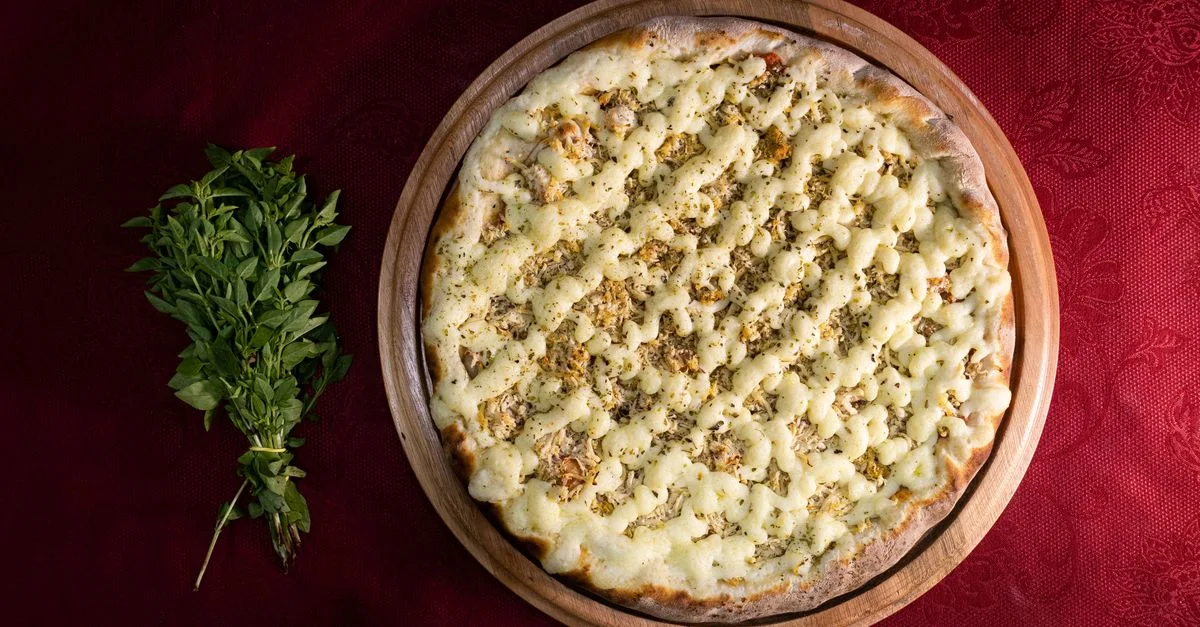 Vista desde arriba de una pizza italiana cargada de queso con hierbas frescas en una bandeja de madera, perfecta para los amantes de la gastronomía.