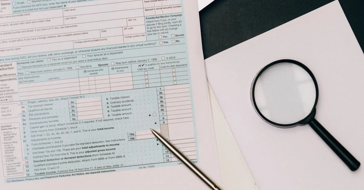 Una vista detallada de un formulario de declaración de impuestos con un bolígrafo y una lupa, perfecto para temas financieros.