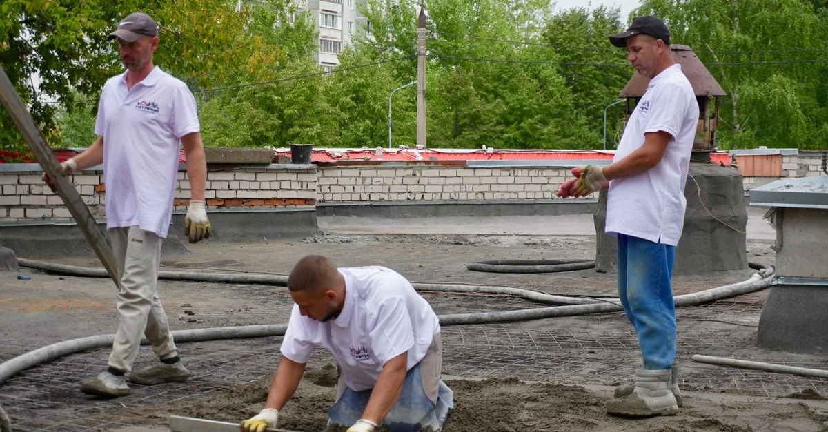 Un equipo de obreros de la construcción vierte y nivela cemento en una azotea.