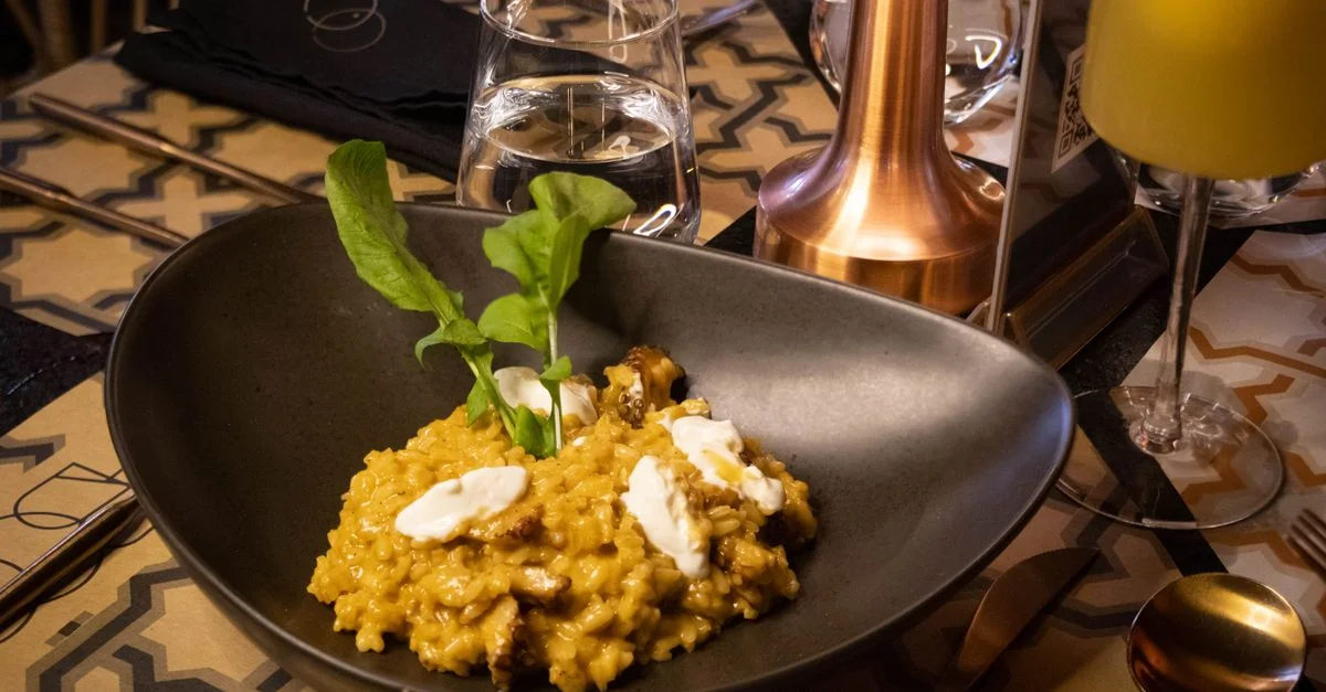 Un lujoso tazón de risotto de champiñones decorado con rúcula, servido en un ambiente de restaurante elegante.