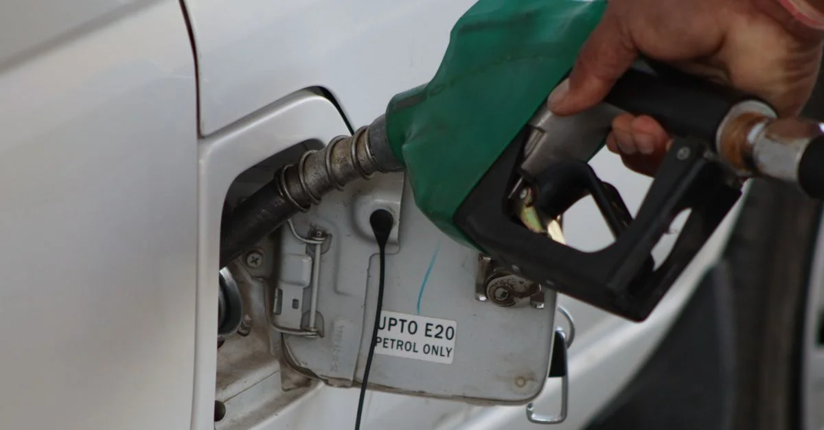 Primer plano de una mano repostando combustible en un vehículo. Boquilla de surtidor de gasolina E20 en uso.
