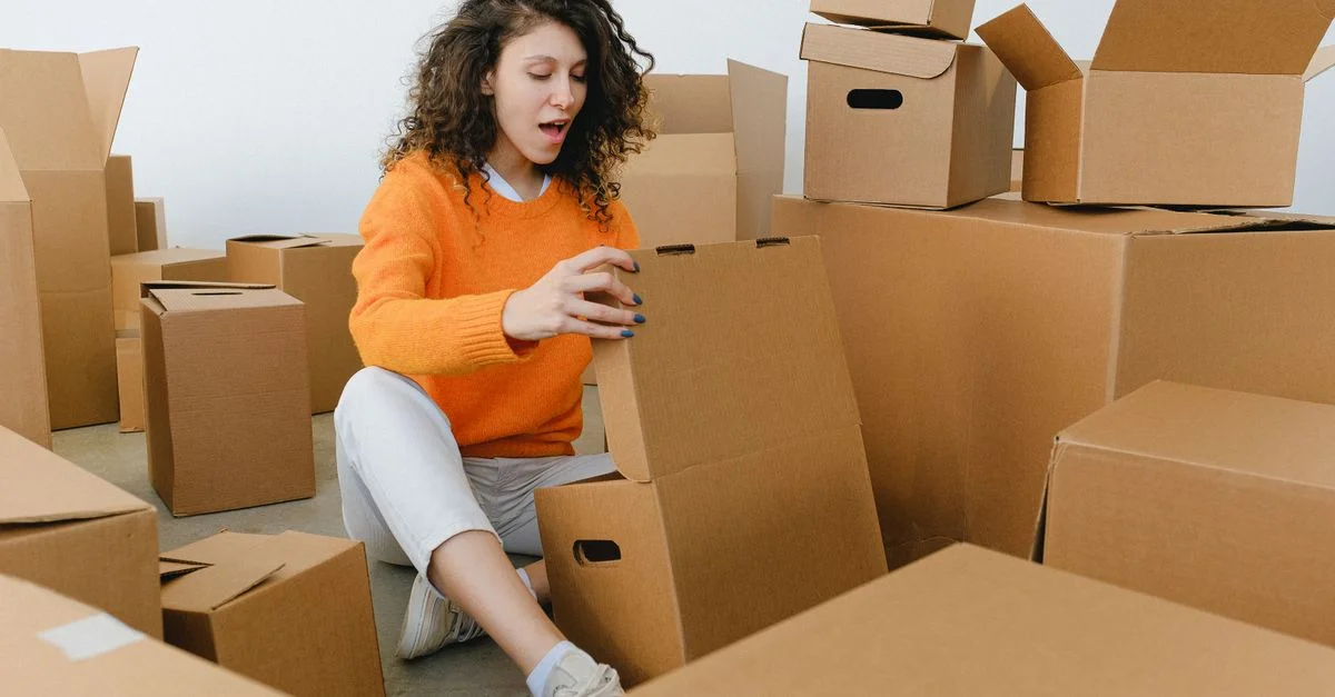 Una joven desempacando con entusiasmo cajas de cartón en su nuevo hogar, rodeada de materiales de embalaje.