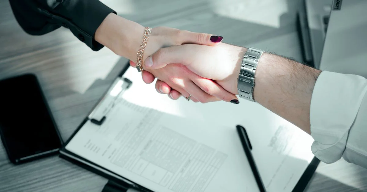 Primer plano de un apretón de manos profesional sobre un contrato, simbolizando un acuerdo comercial exitoso.