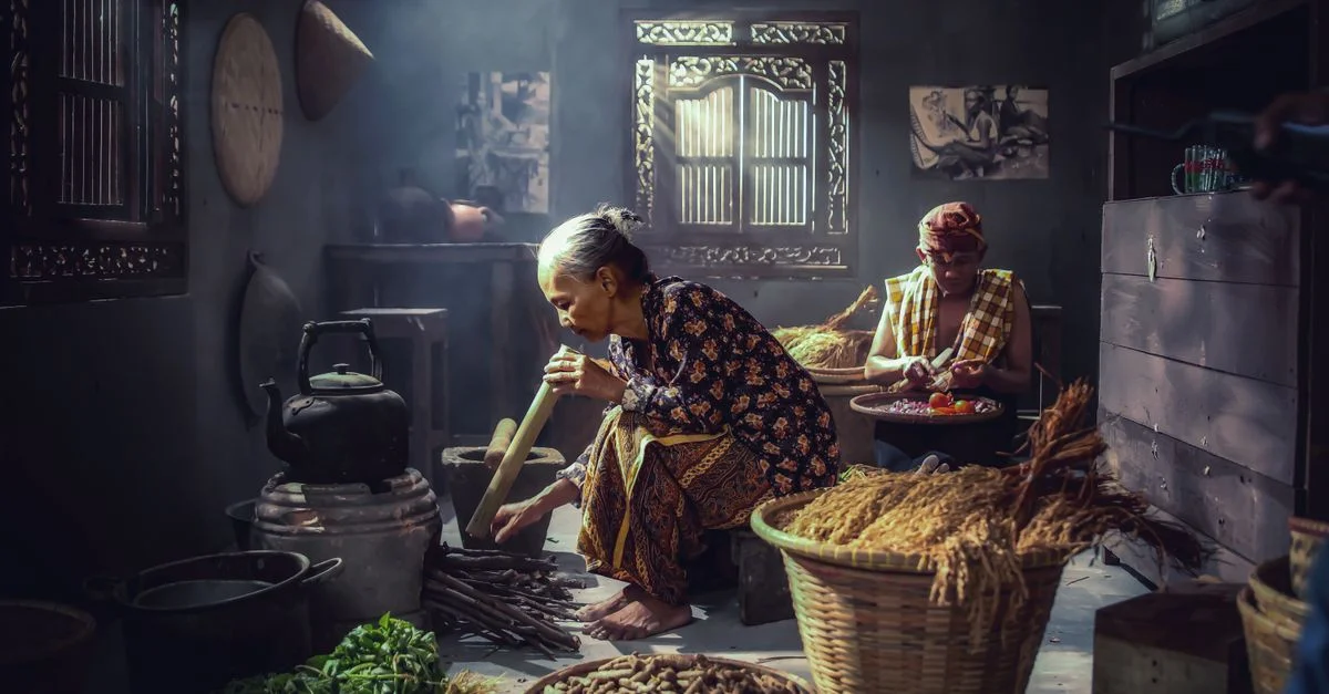 Momento íntimo en una cocina indonesia con dos adultos preparando comida utilizando métodos tradicionales.