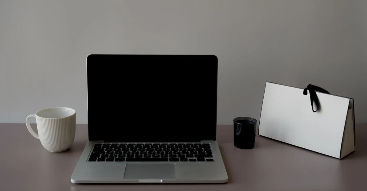 Un espacio de trabajo elegante y minimalista con un portátil, una taza de cerámica y una bolsa de papel estilosa. Perfecto para la productividad.