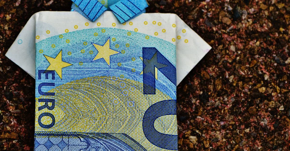 Un billete de 10 euros doblado en una camiseta de origami sobre un fondo texturizado que muestra creatividad.