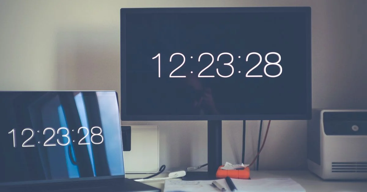 Un escritorio contemporáneo que presenta un portátil y un monitor con pantallas de reloj digital.