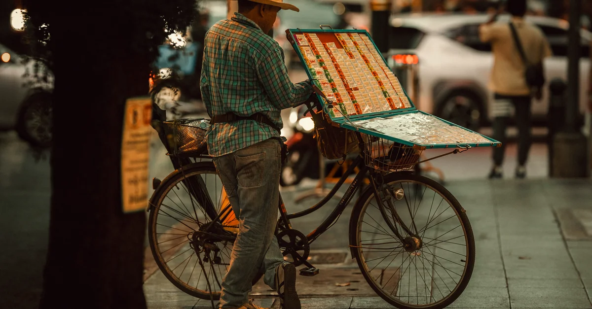 Vendedor ambulante en Bangkok con una bicicleta vendiendo boletos de lotería por la noche.