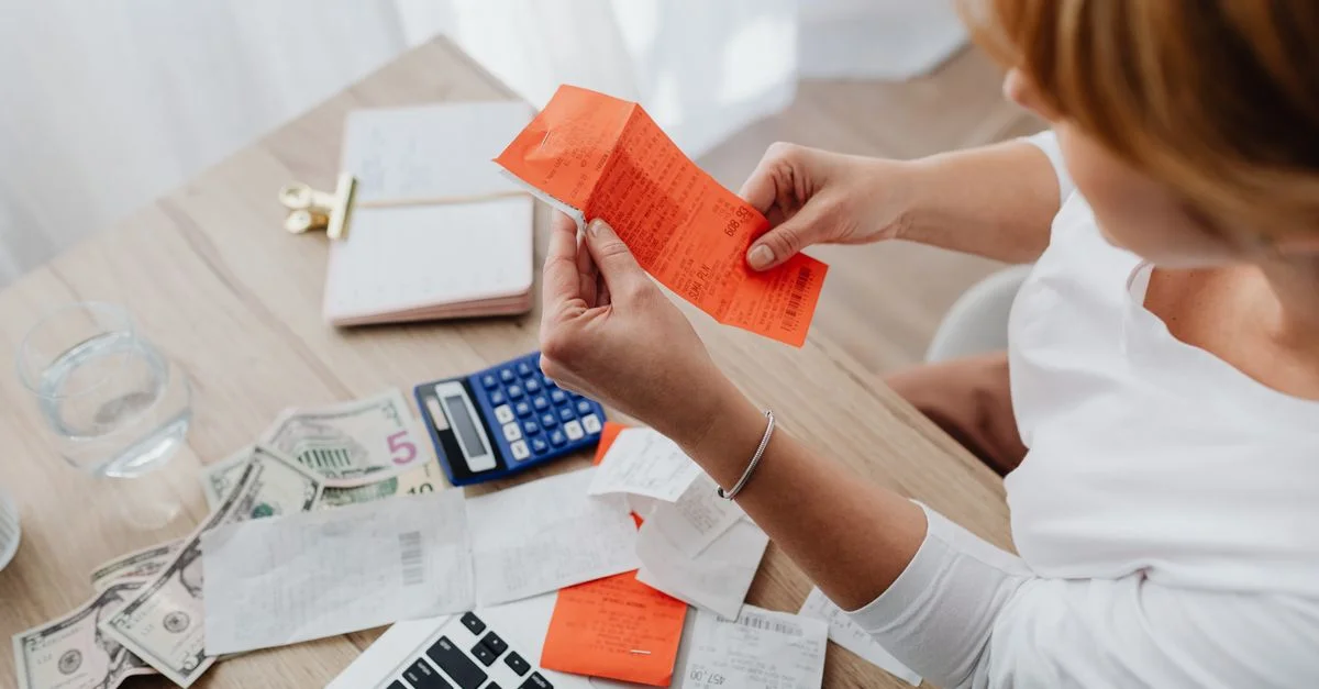 Mujer utilizando calculadora y recibos en el escritorio de la oficina en casa para la gestión financiera.