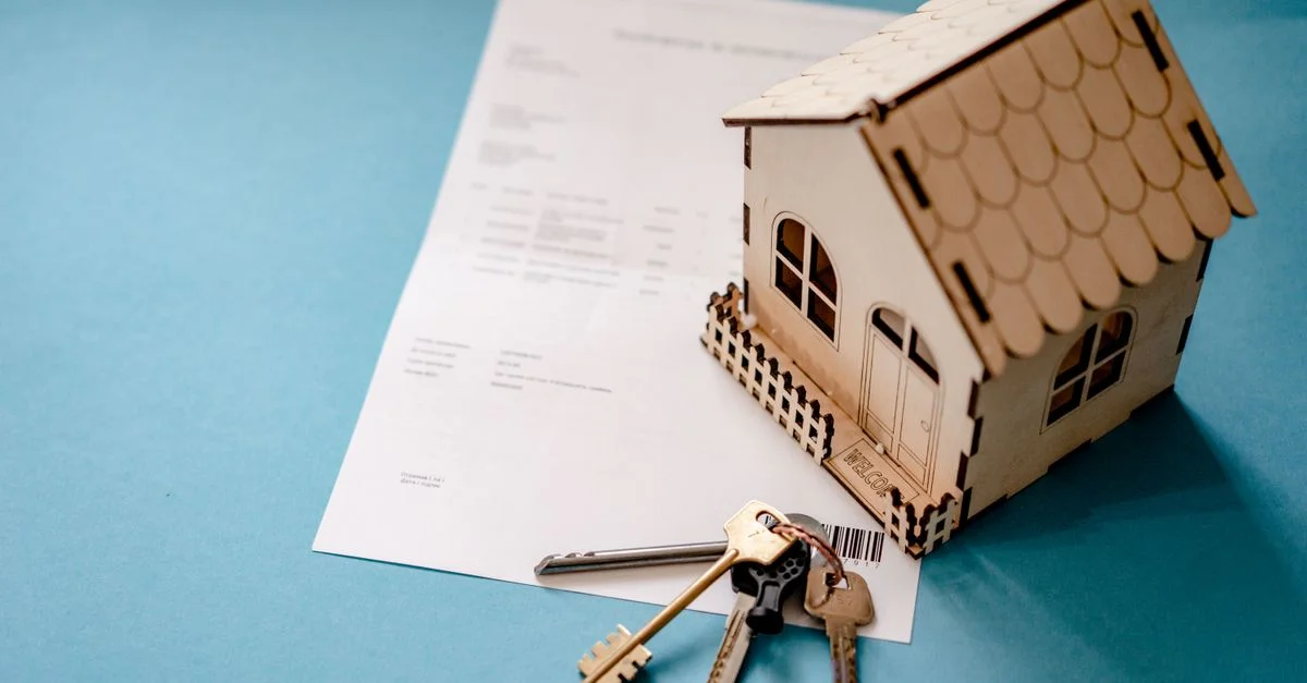 Casa de madera en miniature con llaves y contrato simbolizando transacciones inmobiliarias.