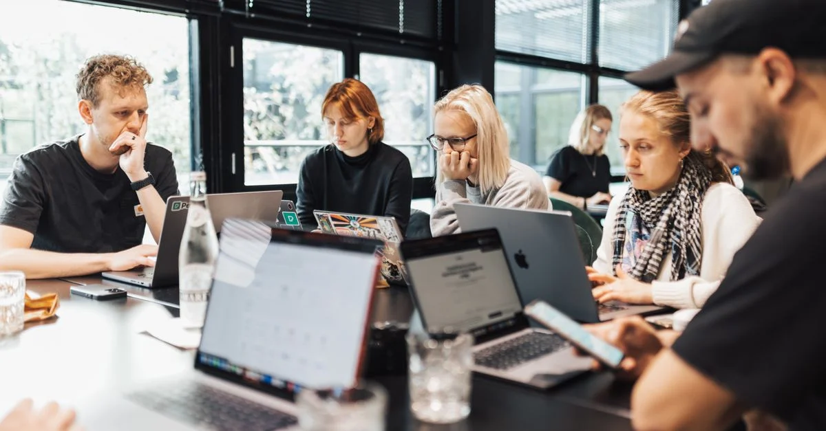 Un grupo de profesionales participando en trabajo digital en laptops y smartphones en un entorno de oficina moderna.