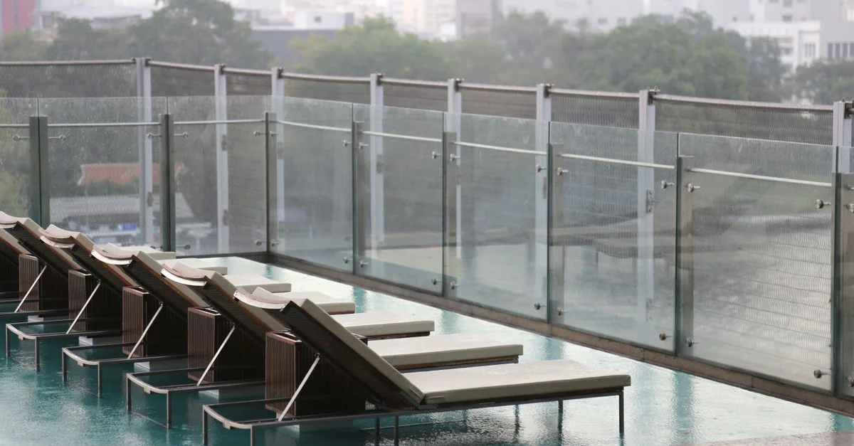 Moderna terraza urbana con tumbonas al lado de una piscina, con barandillas de vidrio.