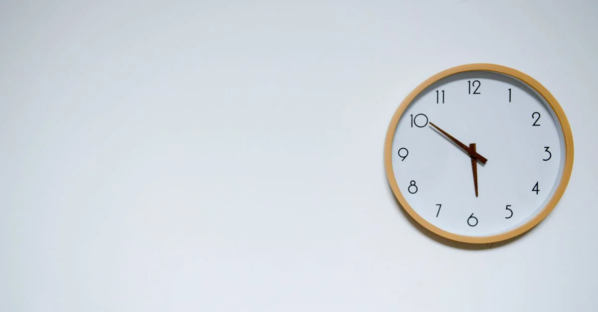 Reloj de pared simple con marco de madera sobre un fondo blanco, mostrando la hora 10:10.