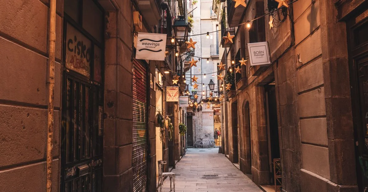 Vista cautivadora de un estrecho callejón de Barcelona adornado con luces de cadena en forma de estrella y fachadas encantadoras.