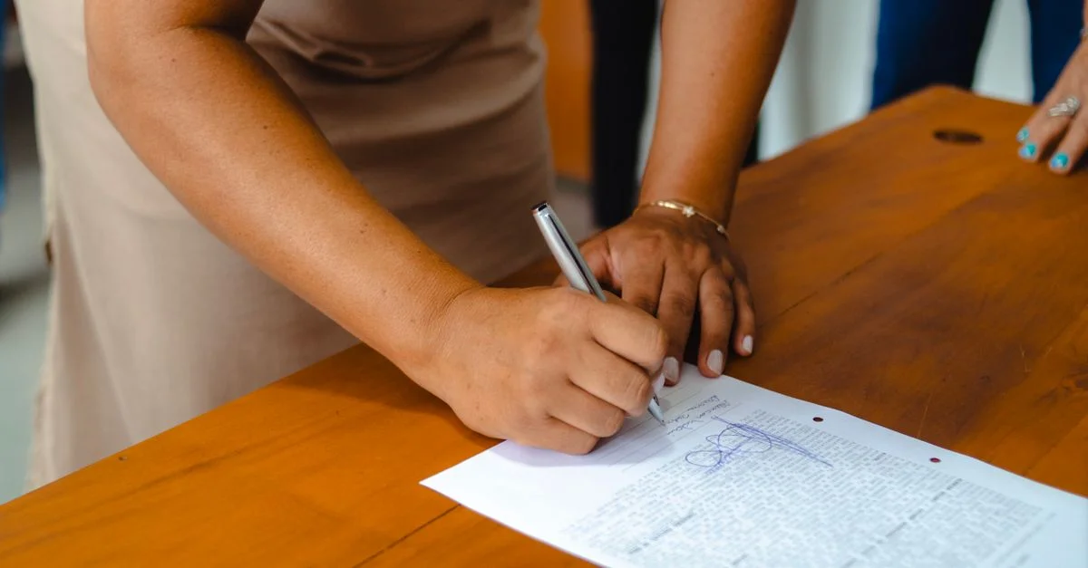 Una mujer profesional firmando un documento oficial en una mesa de madera en interiores.