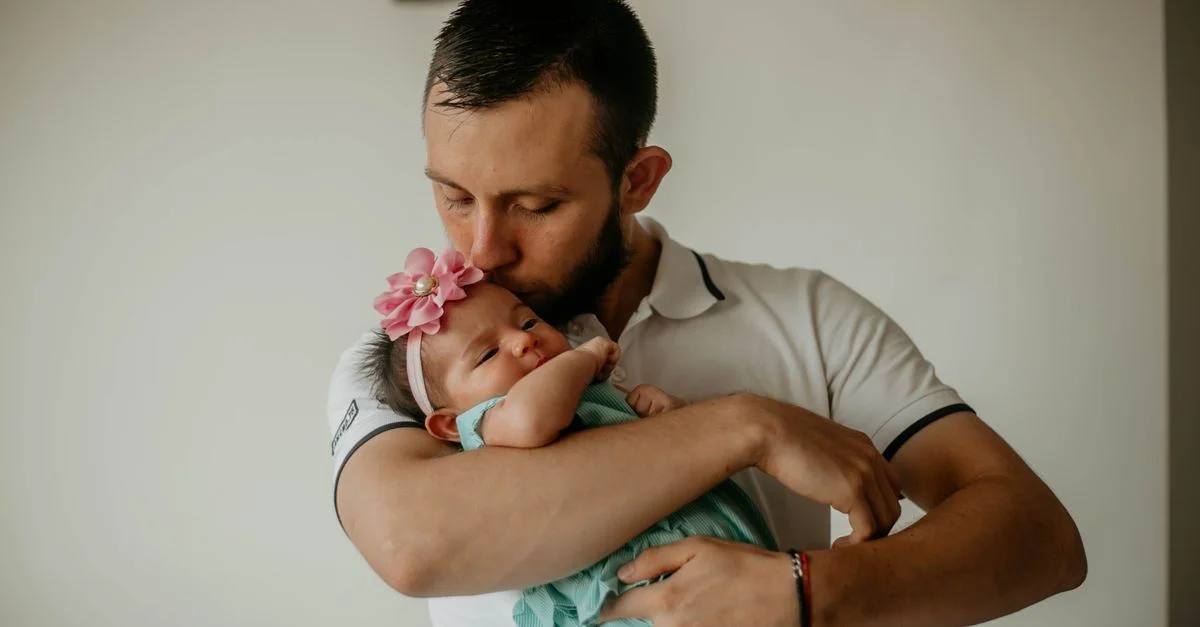 Momento tierno de un padre sosteniendo y besando a su bebé hija en interiores.