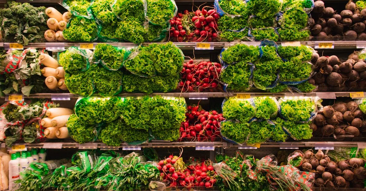 Colorida variedad de verduras frescas organizadas en estanterías de supermercado, perfectas para temas de alimentación saludable.