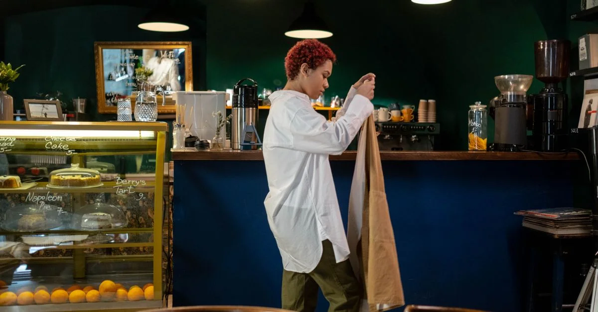 Una barista se pone un delantal en una cafetería acogedora, lista para los clientes.