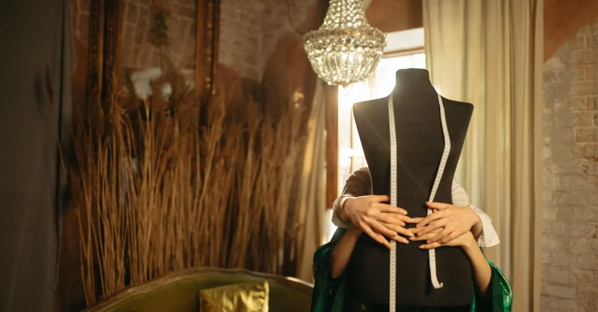 Un elegante taller de moda con un maniquí, sofá vintage y una lámpara de araña ornamental, creando un ambiente acogedor.