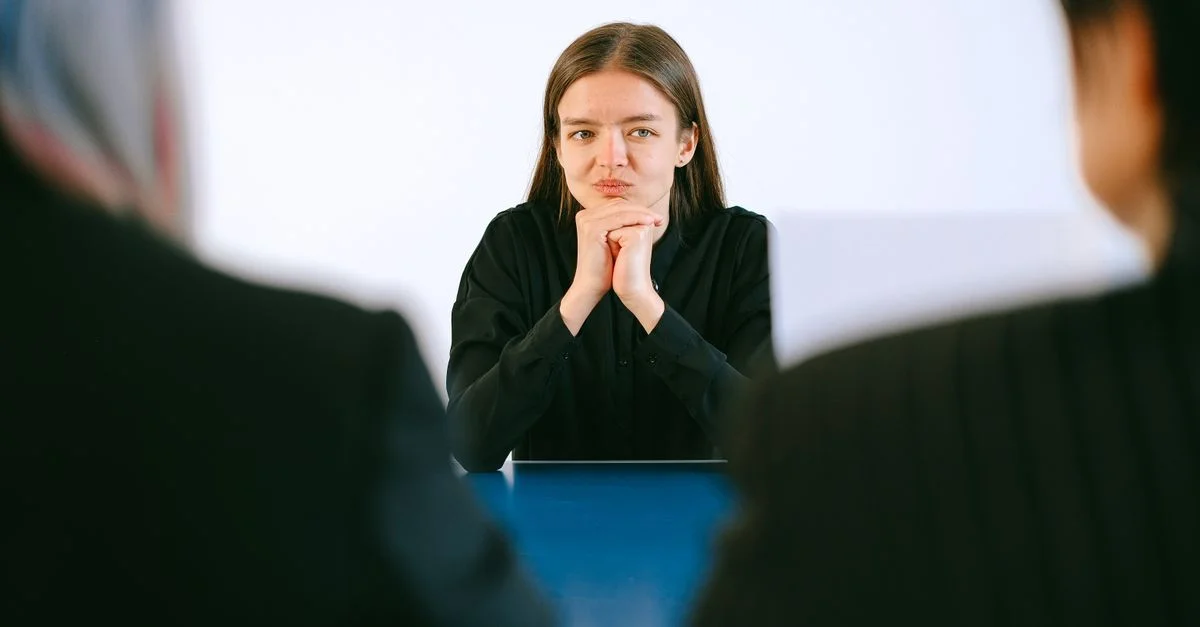 Una mujer en una entrevista de trabajo frente a dos personas en una mesa de oficina, concentrándose intensamente.