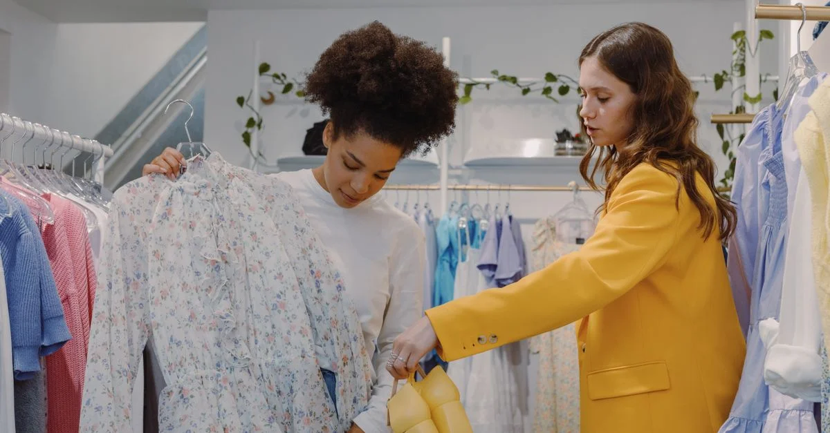 Dos mujeres de compras de manera elegante en una boutique chic con ropa floral y amarilla.