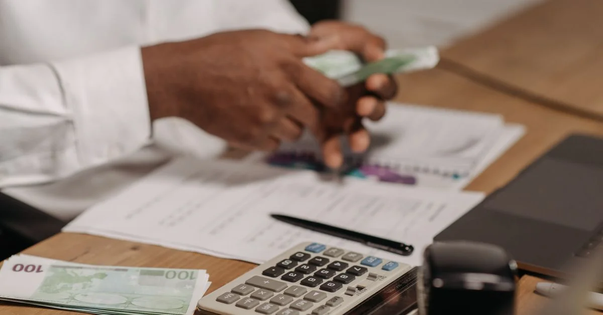 Manos contando billetes de euro sobre un escritorio de madera con calculadora, documentos financieros y laptop cerca.