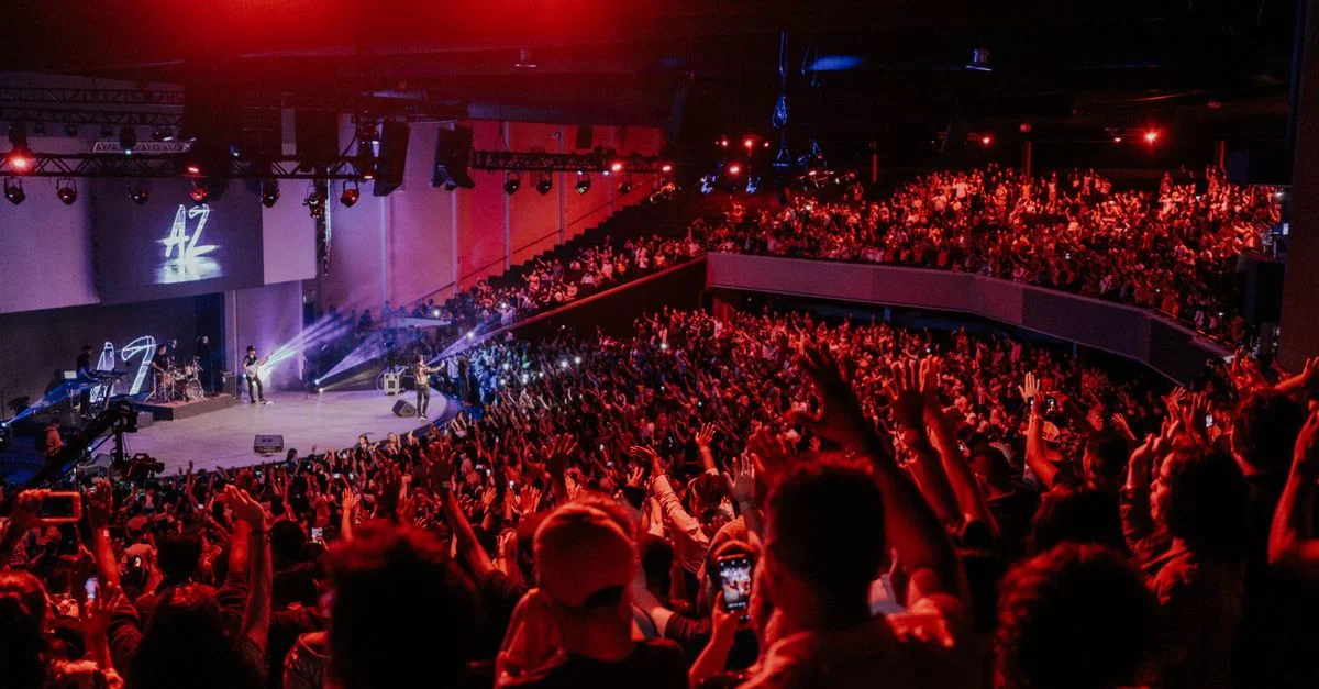 Escena vibrante de concierto en vivo con una multitud emocionada bajo una iluminación dramática en el escenario.