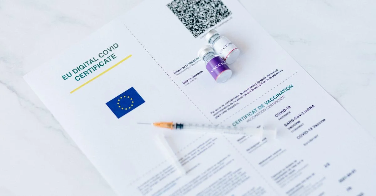 Certificado digital de COVID de la UE con frascos de vacuna y jeringa sobre un fondo blanco.