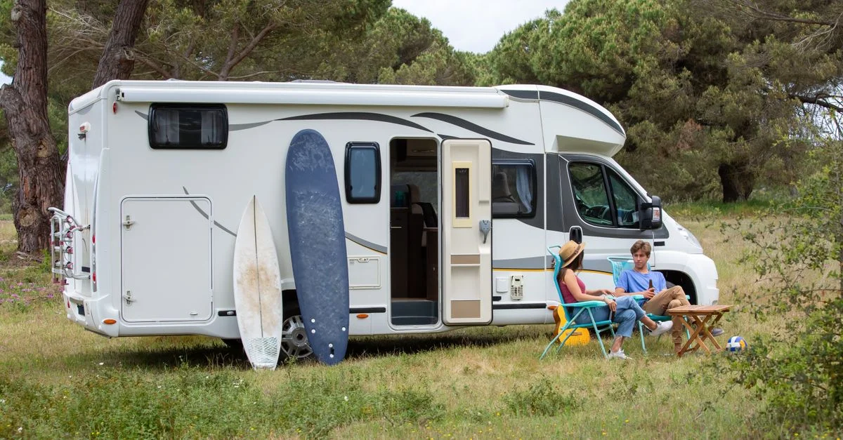Una pareja se relaja fuera de su autocaravana con tablas de surf en un camping pintoresco en Portugal, disfrutando de unas vacaciones de verano.