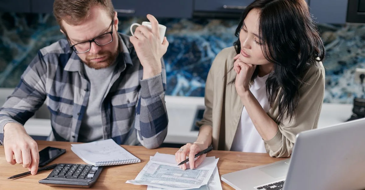 Una pareja revisa facturas y documentos en un portátil mientras discute las finanzas del hogar.