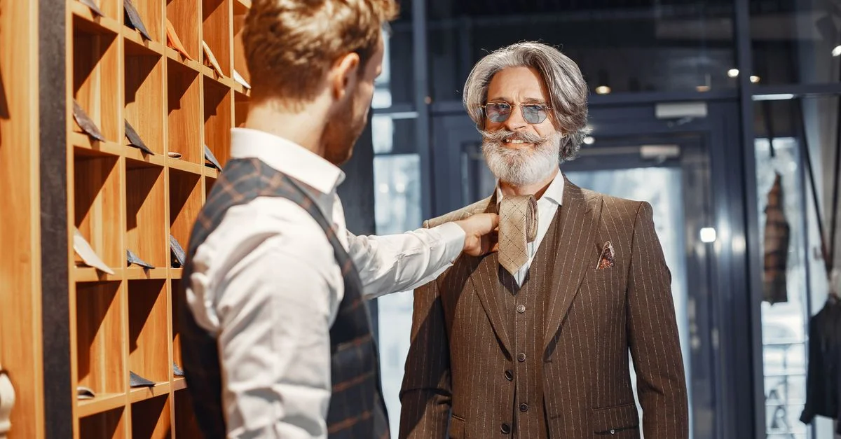 Caballero anciano probándose un traje con ayuda en una tienda elegante. Ambiente elegante y formal.