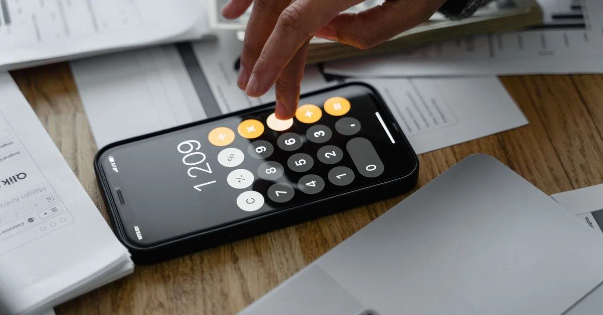 Primer plano de una persona usando una calculadora de smartphone sobre una mesa con documentos para cálculos financieros.