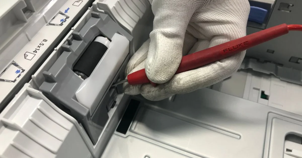 Una mano con guante repara una impresora utilizando una herramienta de precisión roja, mostrando habilidades de mantenimiento.