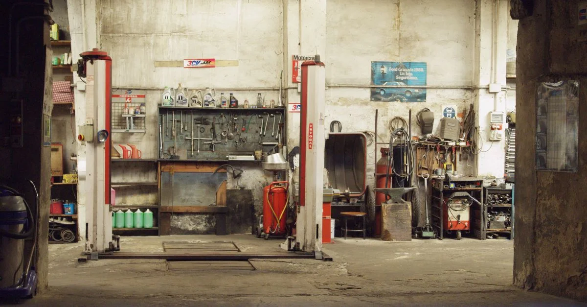Un taller de automóviles vacío y rústico con herramientas, maquinaria y elevadores de automóviles en un entorno industrial.