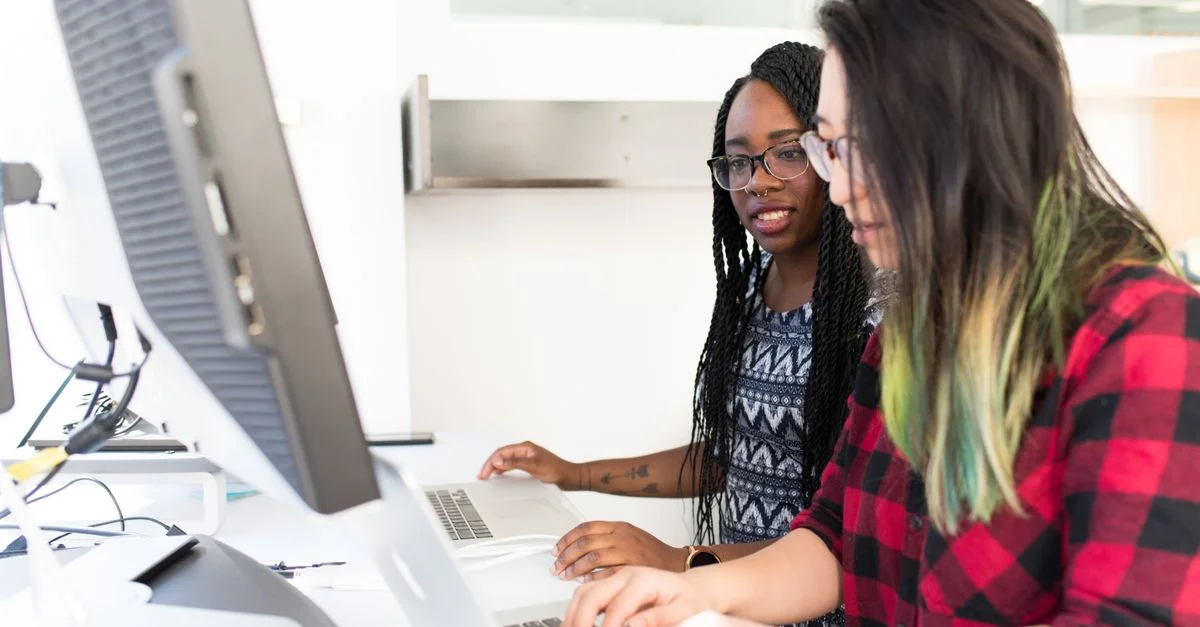 Dos mujeres trabajando juntas en laptops en un espacio de oficina moderno y luminoso.